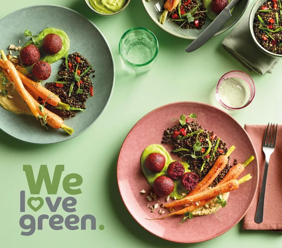 Ein Aktionsbild zu we love green. mit Tellergerichten mit viel Gemüse auf einem grünem Tisch