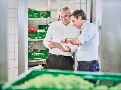zwei Männer stehen in einem kühllager für Obst und schauen zusammen auf ein Tablet