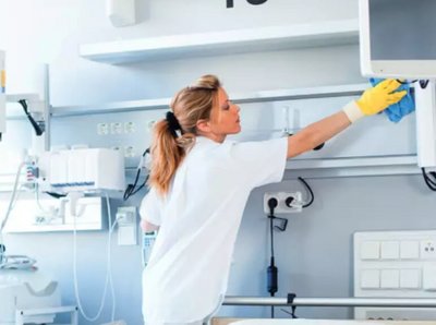 eine Frau reinigt in gelben Gummihandschuhen und einem blauen Tuch ein Krankenhauszimmer