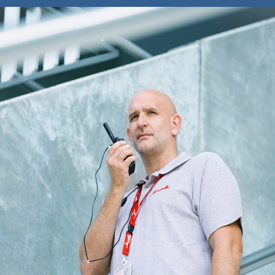 Eine männliche Sicherheitskraft hält ein Walkie-Talkie in der Hand und scheint eine Nachricht abzuhören.